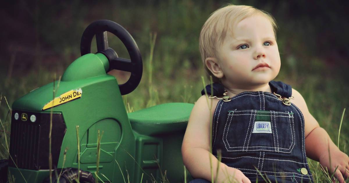 Farm Kids | A photograph of a small child sitting in a field with a green toy tractor. | Harrowsmith Magazine